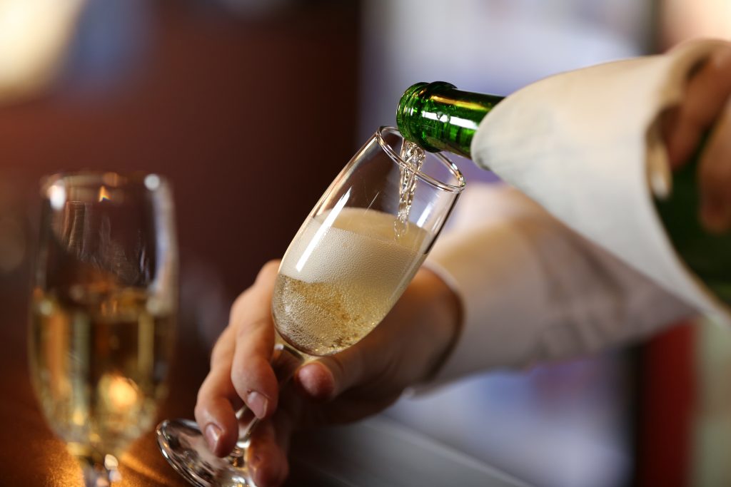 Server pouring Champagne into flute, napkin over the bottle