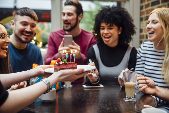 Five friends at a restaurant while a server brings over a birthday cake with candles