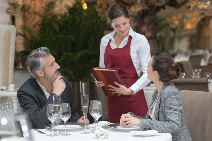 Female server at a fine dining restaurant approaches table with a couple sitting down