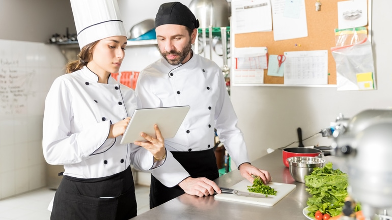 Dos cocineros usando una tableta en la cocina de un restaurante