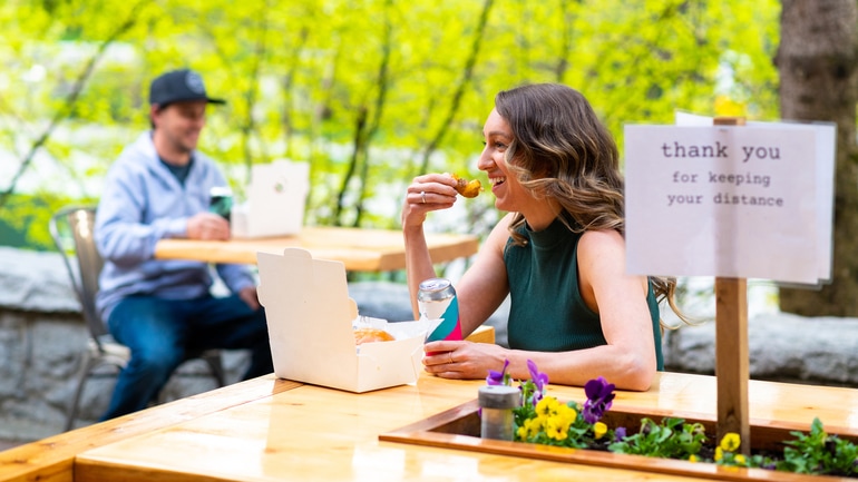 Woman and a man dining outside at separate tables.